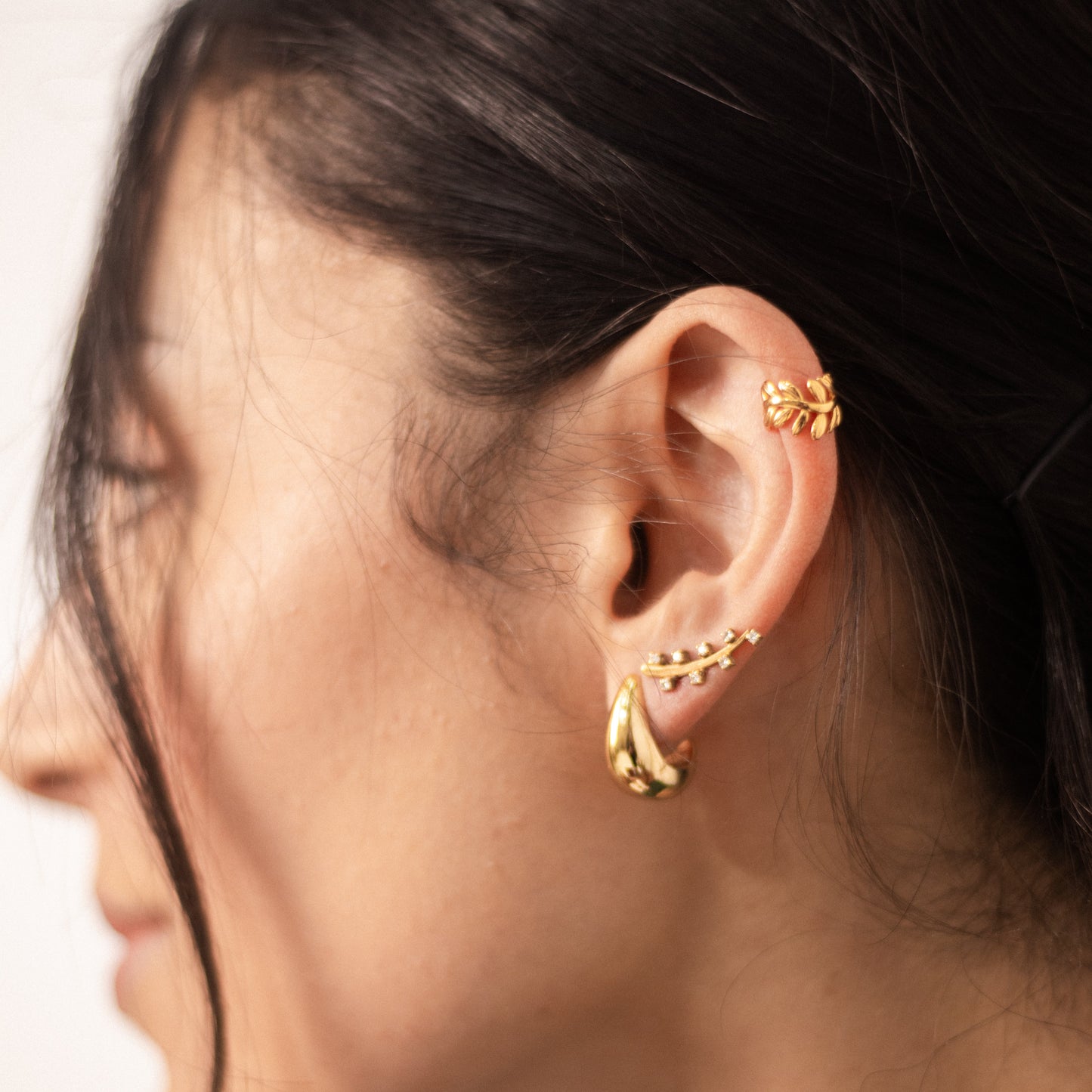 A model wearing a gold ear cuff with olive leaves.