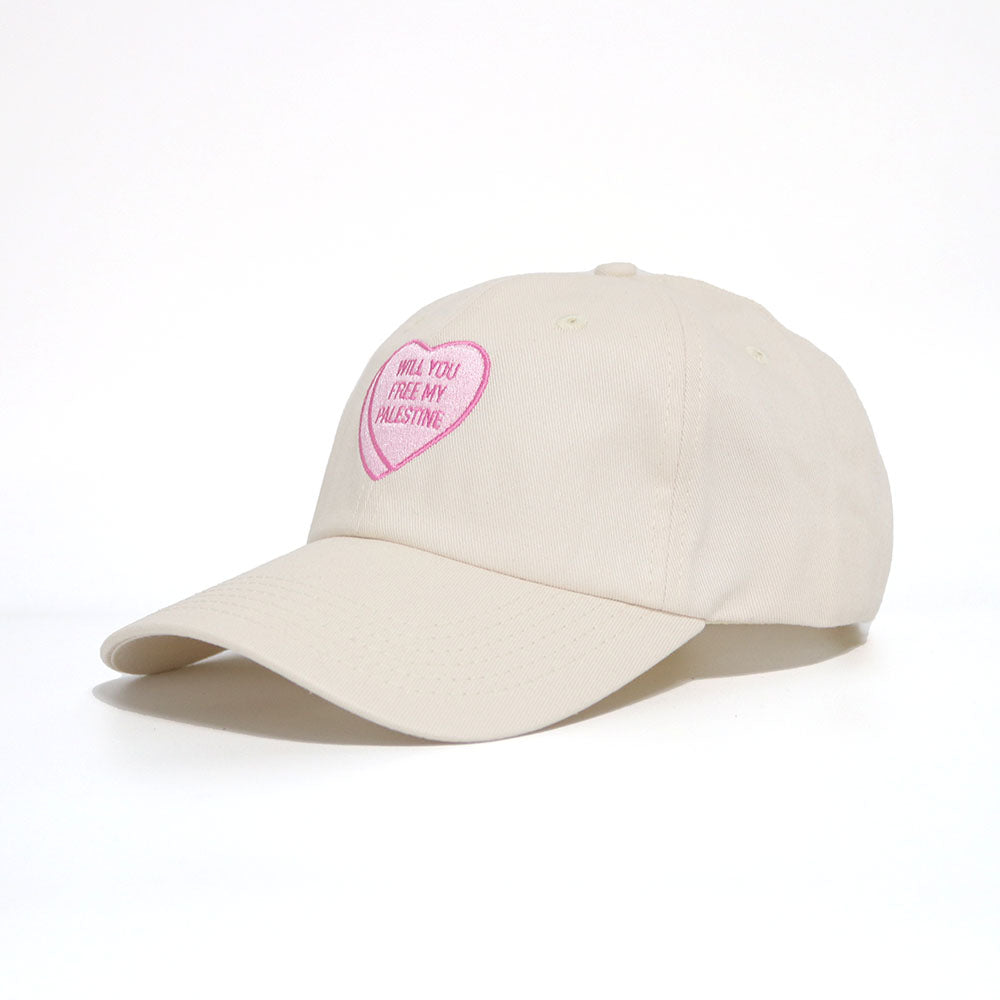 Off-white dad hat with a pink heart, similar to candy hearts, with the text 'will you free my Palestine'. 