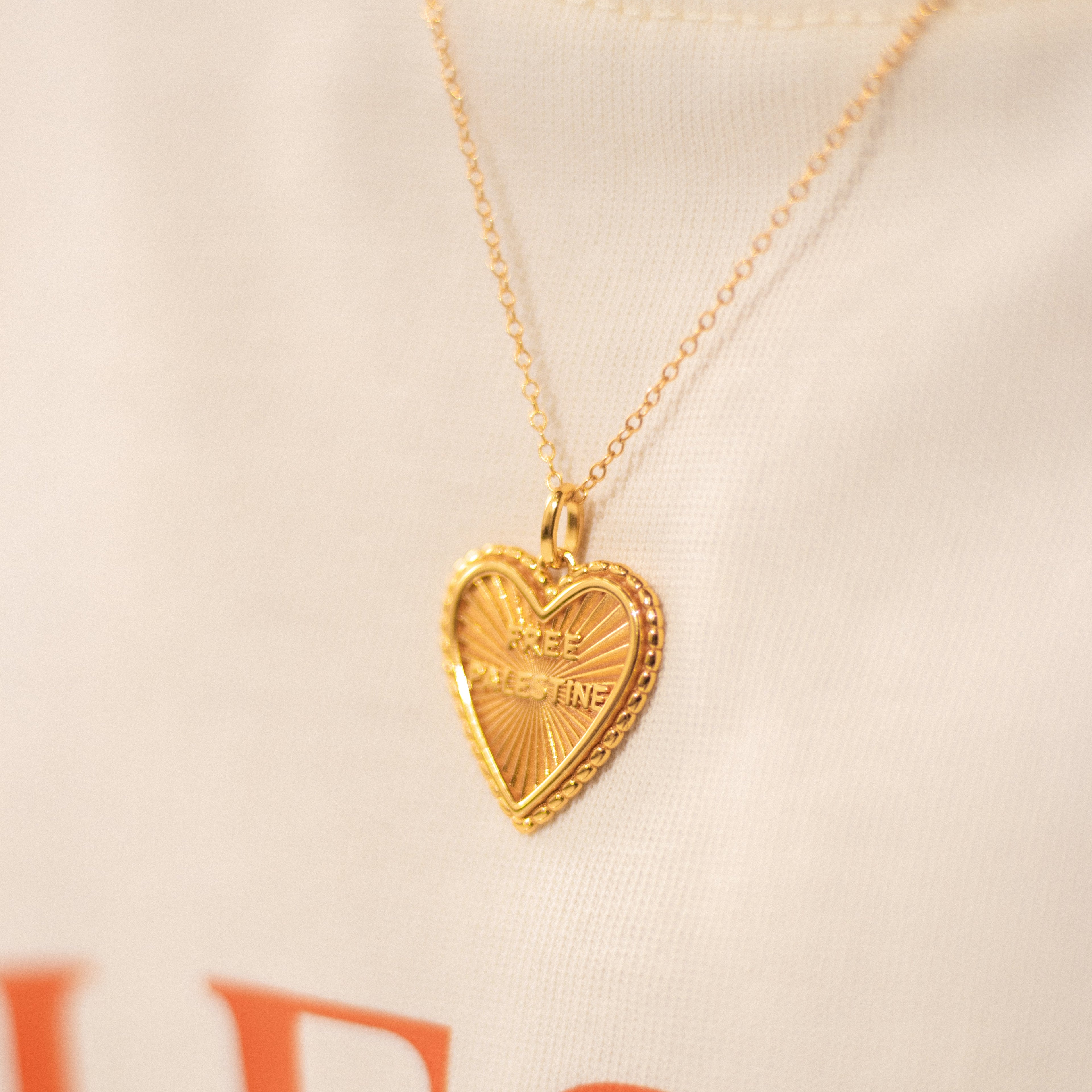 Image shows a gold pendant necklace. The pendant is a heart shape with the text 'Free Palestine'.