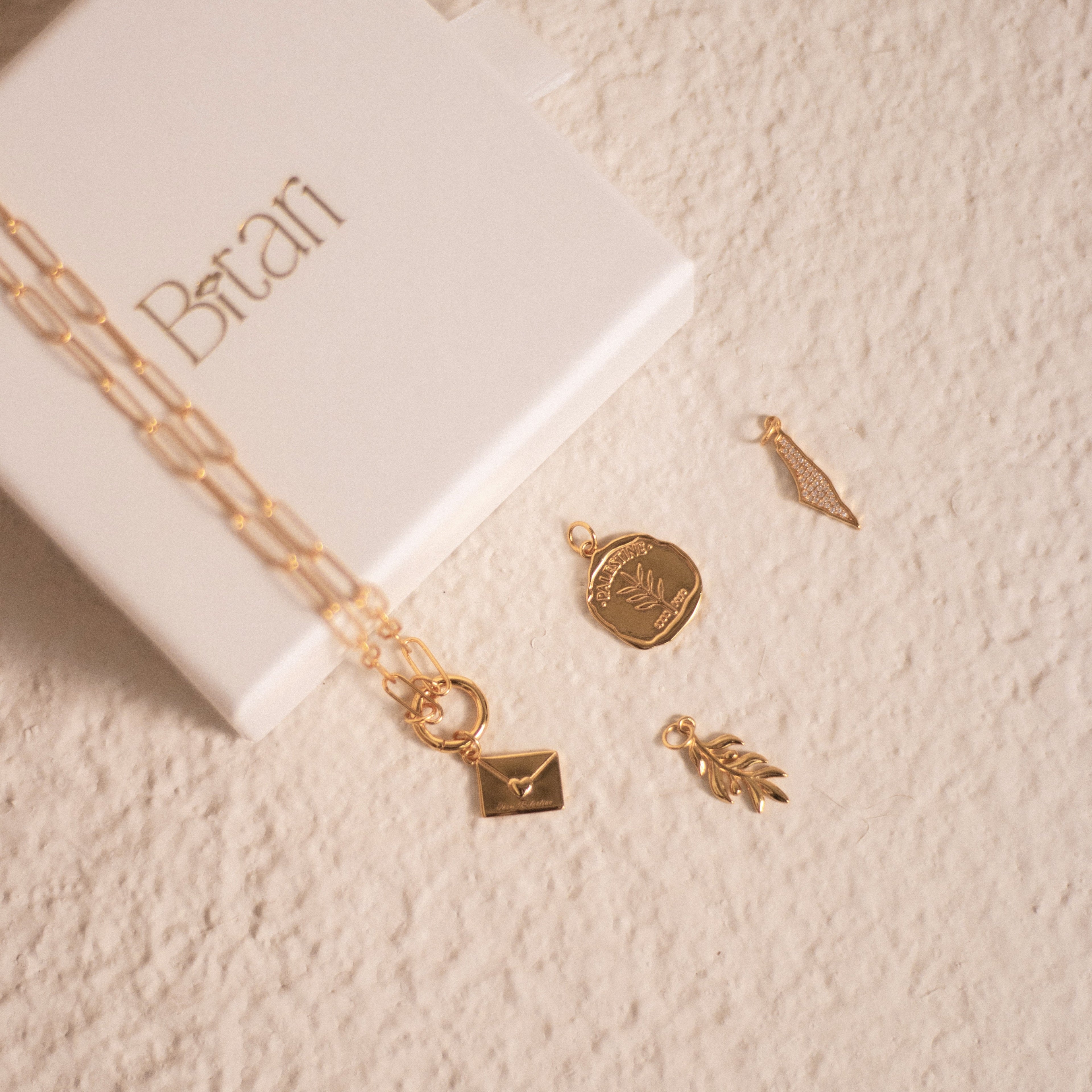 Image showing 4 charms, one Palestine coin, one envelope with the text 'From Palestine', one Palestine map and one olive branch.