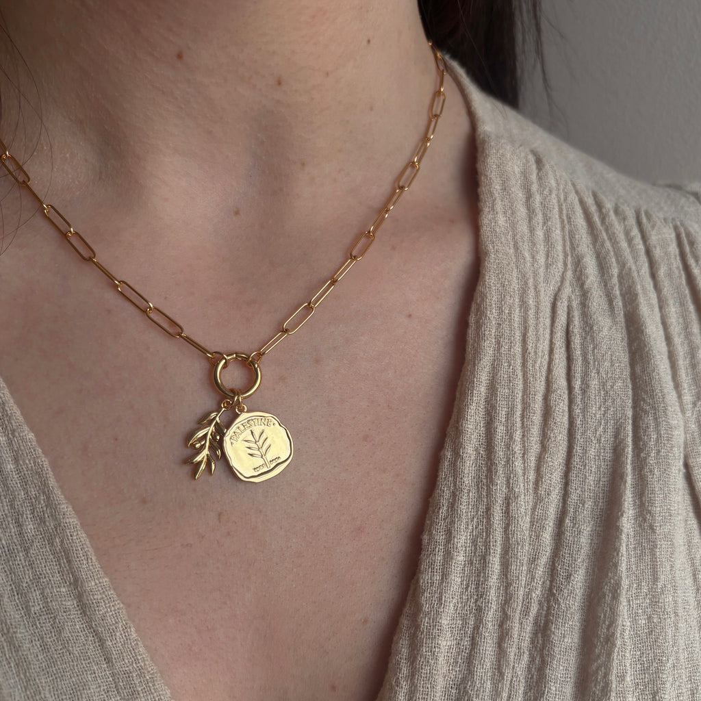 Gold paperclip chain necklace with two charms, one Palestine coin and one olive branch.