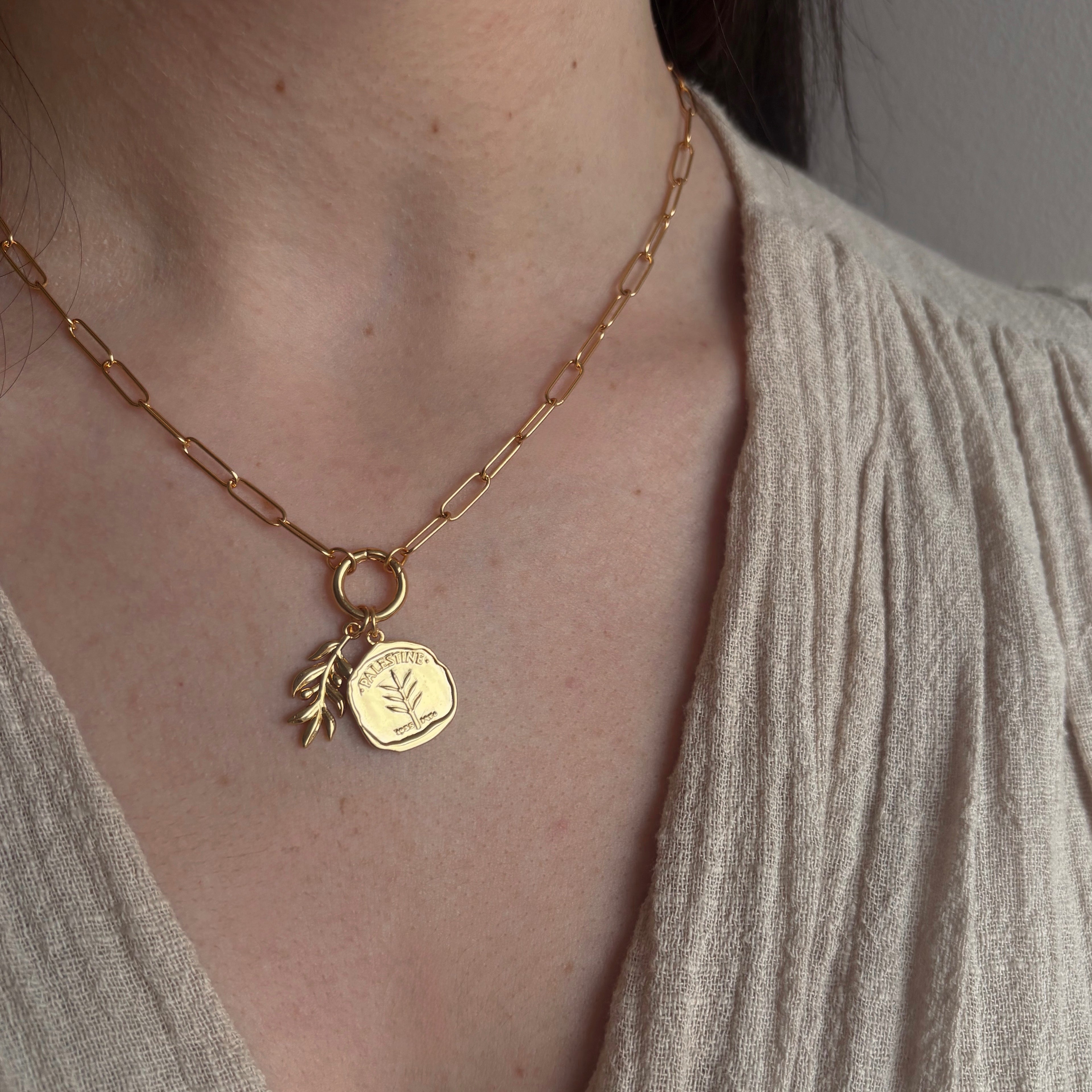 Gold paperclip chain necklace with two charms, one Palestine coin and one olive branch.