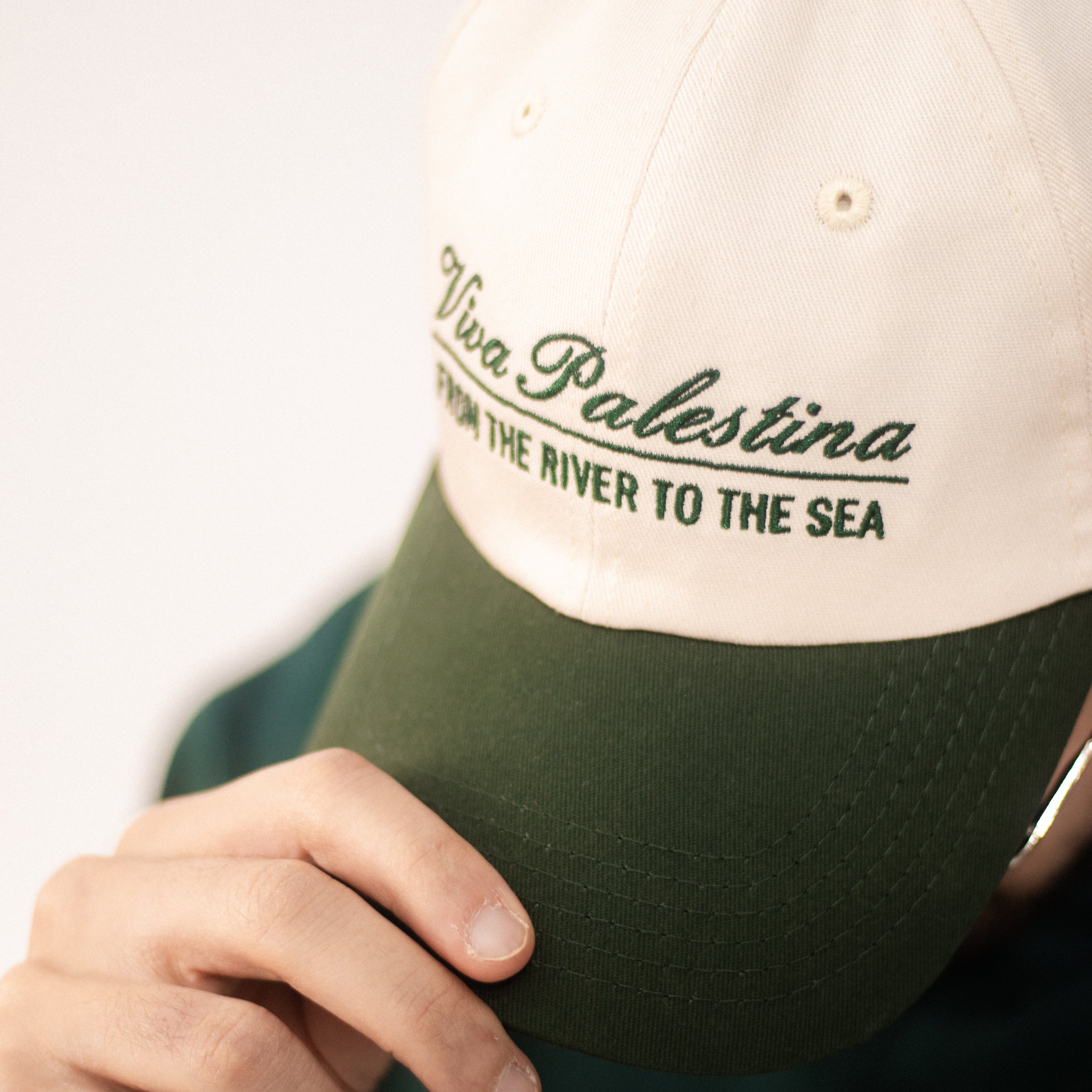 Model wearing an off-white and green dad hat with with the text 'Viva Palestina, From the river to the sea' embroidered in green.