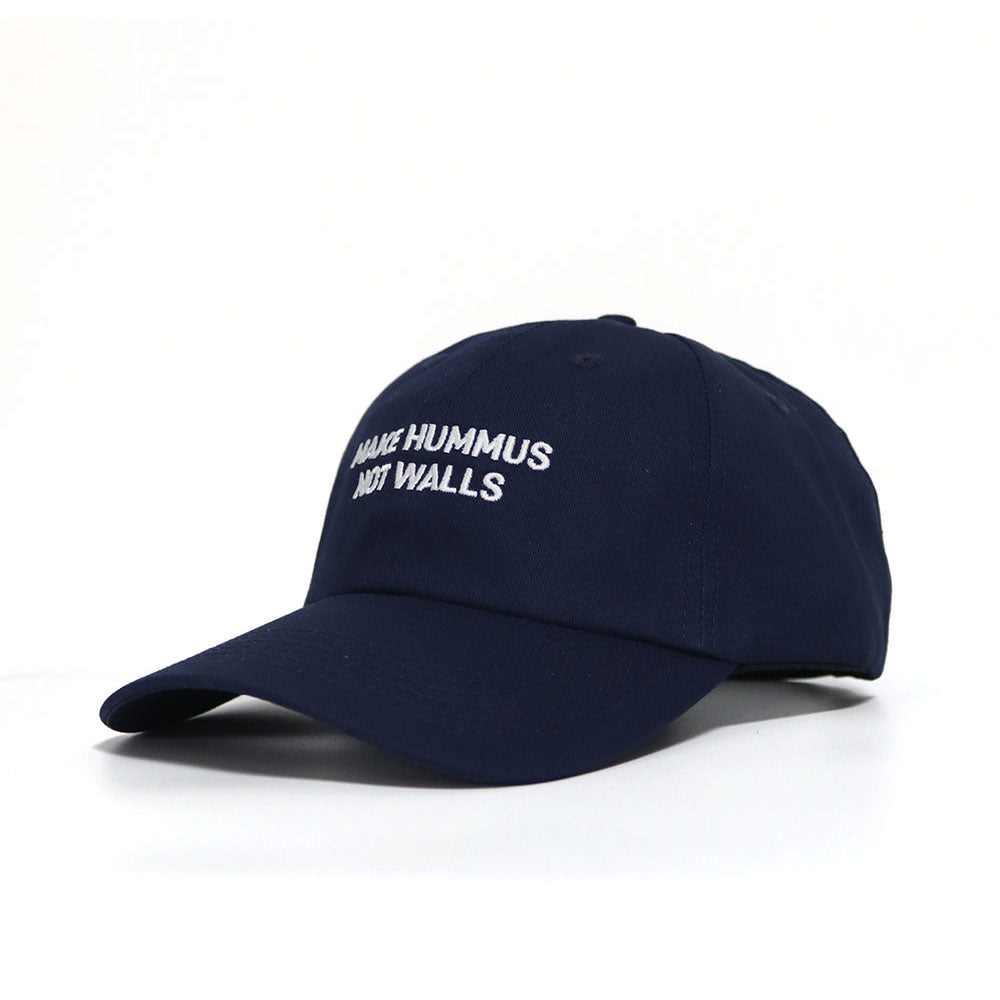 A blue dad hat with with the text 'make hummus not walls' embroidered in white.